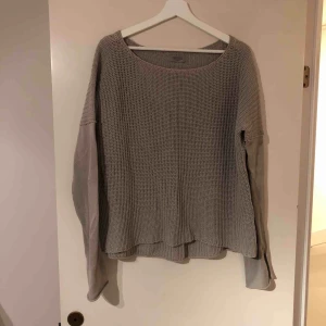 - Stickad tröja från Hunkydory i ljusgrå färg och skönt bomullsmaterial. Sitter väldigt löst och har lågt hängande axlar. Urringningen börjar där nyckelbenet möter resten av axeln. Ärmarna är lite längre och ryggen går nästan förbi rumpan. 