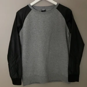  - Sweatshirt från Urban Classics som tyvärr aldrig kommer till användning. Grå med ärmar i fejk-skinn. Som ny ✨ Köparen står för eventuell frakt!