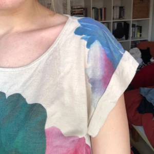  - Beige t-shirt med stort färgglatt mönster. Köparen betalar frakt. 