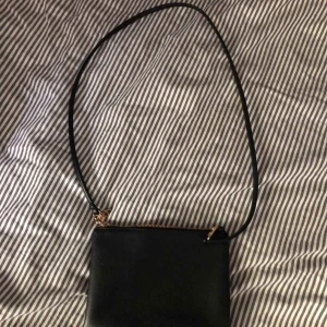  - Liten enkel väska i svart läderimitation och med guldiga detaljer. Bandet är tunt och kan tas av. fraktkostnad tillkommer