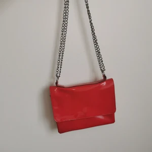 Röd vinyl väska - Super fin väska från monki. Kedjan går att göra så att det är antingen en axelväska eller crossbody. 3 fack + ett litet. 2 av dom med dragkedja. 