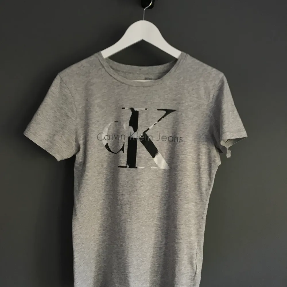 Grå t-shirt med silver/svart tryck från Calvin Klein. Storlek S. Fint skick. . T-shirts.