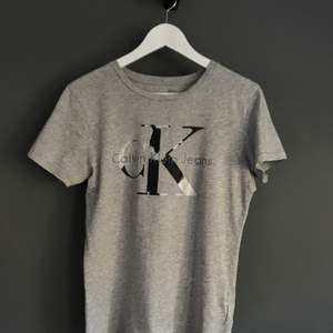 Grå t-shirt med silver/svart tryck från Calvin Klein. Storlek S. Fint skick. 
