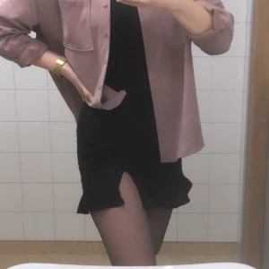 Svart kjol med slit - Svart kjol med volang längst ner och slit på vänsterbenet. Bara använd en gång så som ny Har ett linne liknande tyg och en innerkjol🦋