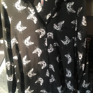 Skjorta - Fin skjorta med katter på - Tunt och bekvämt material. Jag har i vanliga fall storlek M i tröjor/klänningar mm, men dessa passar mig bra (har även lite större byst som den sitter fint på). Knappt använd.