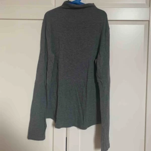  - En mörkgrå långärmad tröja som har en liten krage. Ärmarna är som du ser längre än vanliga långärmade tröjor. Tröjan är även stretchig.