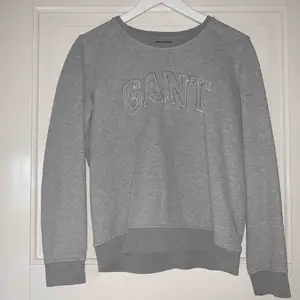 Grå sweatshirt från GANT som är väldigt skön men sällan använd. Stort tryck på framsidan, inga överisa detaljer. Fler bilder kan skickas, frakt ingår ej.