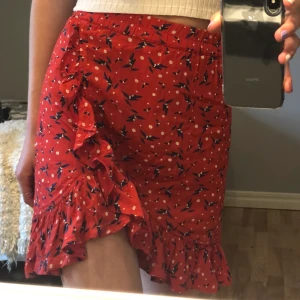 Somrig kjol - Röd kjol med vita och blåa detaljer. Köptes förra året och har bara använts 3 gånger Väldigt skönt material men säljer då den är för stor i midjan. Köparen står för frakten.