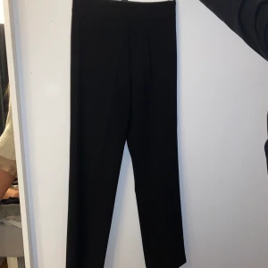 Svarta kostymbyxor - Svarta vida kostymbyxor från Chiquelle. Hög midja och en ”fejk” kostymficka bak. Försluts med en dragkedja i sidan. Möjligen något stora i storleken, passar även 38.