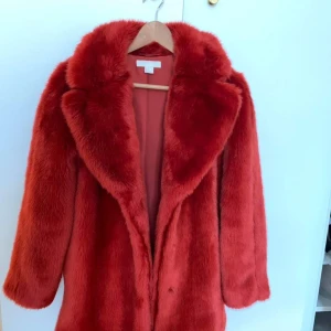 Röd fuskpäls i st 38 - Saknas en knapp.finns att hämta på gärdet eller levereras. 