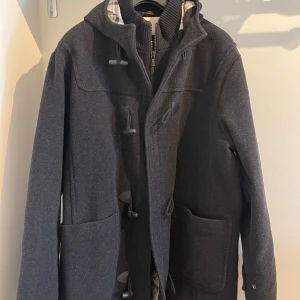 Grå duffel från Henri Lloyd - Säljer en snygg och stilren grå duffel från Henri Lloyd. Jackan har en klassisk design med en dragkedja för extra värme. Den är långärmad och har en huva för att skydda mot väder och vind. Perfekt för höst och vinter! I använt bra skick.