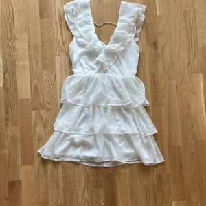 Vit klänning från Eve - Säljer en superfin vit klänning från Nelly i storlek 34. Den har en härlig volangdesign med flera lager och en v-ringad hals. Perfekt för sommarens alla fester! 💃