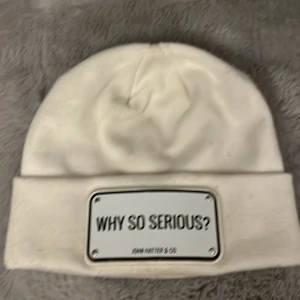 JOHN HATTER & CO MÖSSA  - En vit vinter mössa från John hatter med texten: why so serious. Använd men inget som märkts särskilt mycket