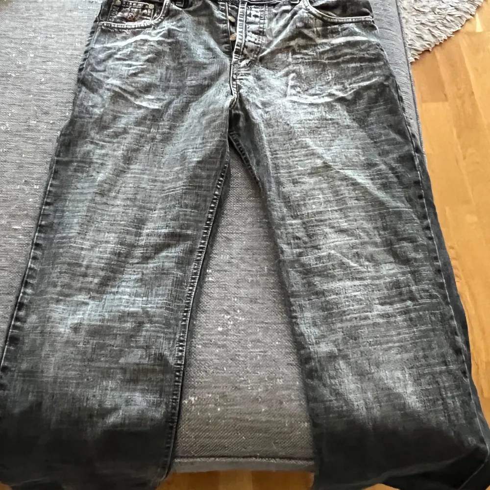 Säljer ett par grå jeans från Dolce & Gabbana. De har en cool, sliten look med ljusa tvättade detaljer. Jeansen har knappar framtill och klassiska fem fickor. Perfekta för en avslappnad stil!. Jeans & Byxor.