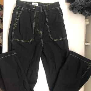 Svarta byxor från Junkyard med gröna sömmar - Säljer ett par svarta byxor från Junkyard i storlek S. De har coola gröna sömmar som verkligen poppar och ger en unik look. Byxorna har en straight leg (?) passform och är perfekta för vardagsbruk.