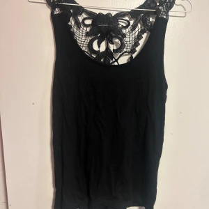 Svart linne med spetsdetaljer - Säljer ett snyggt svart linne med vackra spetsdetaljer vid halsen och ryggen. Linnet har en unik snörning på baksidan som ger en extra touch. Perfekt för en utekväll eller fest! 🖤