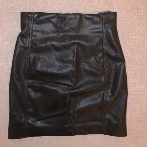 Svart skinnkjol från H&M - Säljer en snygg svart skinnkjol från H&M. Kjolen är i kort modell, gjord i ett läderliknande material. Knappt använd så i väldigt fint skick 