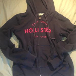 Hollister Hoodie - En jätte gullig Hollister hoodie med rosa text, står storlek L men är ganska liten för sin storlek. Jätte fin och är i bra skick, säljer då jag har flera liknande så denna används aldrig.