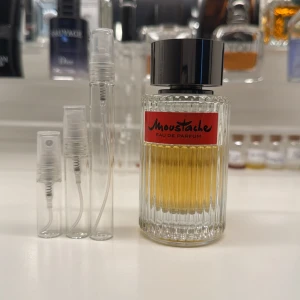 Moustache Eau de Parfum - Parfymen har en varm, gyllene färg och etiketten är röd med svart text. Perfekt för den som vill ha en klassisk doft. 