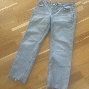 Grå jeans med råa kanter - Säljer ett par grå jeans med en cool, avslappnad stil. De har råa kanter vid bensluten som ger en trendig look. Perfekta för vardagsbruk och kan matchas med nästan vad som helst. De är i bra skick och redo för en ny ägare!