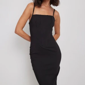 Midiklänning  - Superfin svart midiklänning med korsettband från NA-KD i storlek 36. Aldrig använd, tyvärr för stor, alla lappar kvar. Slutsåld på hemsidan!💗 