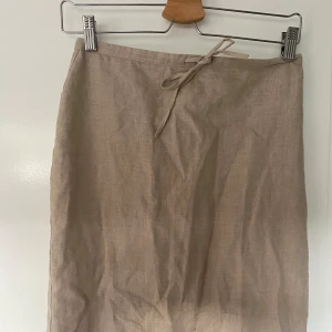 Beige långkjol från Hennes - Säljer en superfin beige långkjol från Hennes i storlek 34. Kjolen är gjord av linne och har en stilren design med knytband i midjan och en slits framtill🙌🏼