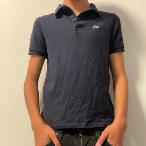 Lacoste Pikétröja  - Hej, säljer nu denna Lacoste piké som har blivit förliten för mig och som jag inte använder. Storleken är 164cm/14 år Modell är 170cm. Tröjan är som nya och har använts fåtal gånger/Abbez Closet🔷