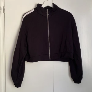 Svart croppad jacka med dragkedja - Säljer en svart croppad jacka från H&M. Den har en dragkedja framtill och en vit rand längs ärmarna. Perfekt för en avslappnad stil och passar bra till både jeans och kjol. Jackan är i bra skick och redo för en ny ägare!