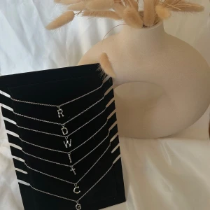 Silverfärgade halsband med bokstavsberlocker - Säljer flera stilrena silverfärgade halsband med olika bokstavsberlocker. Perfekta för att ge en personlig touch till din outfit. Kedjan är tunn och elegant, vilket gör den lätt att bära till både vardags och fest.