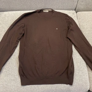 Brun tröja från J.Lindeberg - Säljer en snygg brun tröja från J.Lindeberg. Den är gjord av 100% merinoull vilket gör den supermjuk och perfekt för kyligare dagar. Tröjan har långa ärmar och en liten logga på bröstet. Perfekt för både vardag och lite finare tillfällen!