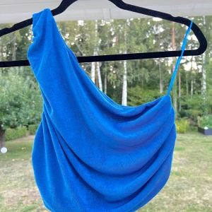 Blå one-shoulder top - Blå stretchig one-shoulder blus 🦋 Dubbelt tyg och inte genomskinlig, kan bäras utan bh! Likadan på framsidan och baksidan, man kan alltså bära den på antingen höger eller vänster axel 💙 Passar till S/M 🥰  (ALDRIG ANVÄND)  Längd: 37 cm Axel: 78 cm
