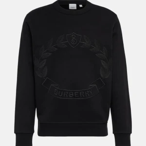 Svart sweatshirt från Burberry - Säljer en stilren svart sweatshirt från Burberry med ett diskret broderat emblem på framsidan. Tröjan har långa ärmar och en klassisk rund halsringning. Perfekt för både vardag och lite finare tillfällen. Superbekväm och lätt att matcha med allt!
