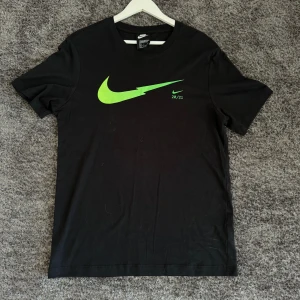 Svart t-shirt från Nike - Säljer en svart t-shirt från Nike i storlek M. Den har en grön Nike-logga på framsidan och är i standard passform. Perfekt för träning eller vardagsbruk!