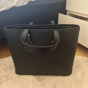 Väska - Säljer denna stilrena vöskan från H&M då den inte kommer till användning längre. Den är i fint skick. Man får plats med väldigt mycket i väskan, som bl.a en dator. 