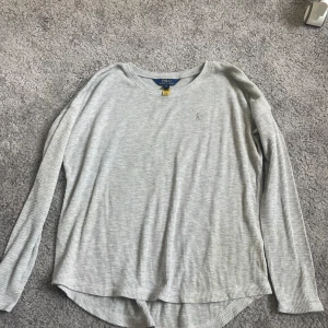 Grå långärmad tröja från Polo Ralph Lauren - Säljer en stilren och bekväm grå långärmad tröja från Polo Ralph Lauren. Tröjan är i ett ribbat material som ger en skön passform. Perfekt för både vardag och avslappnade tillfällen. Passar bra till jeans eller chinos för en casual look.