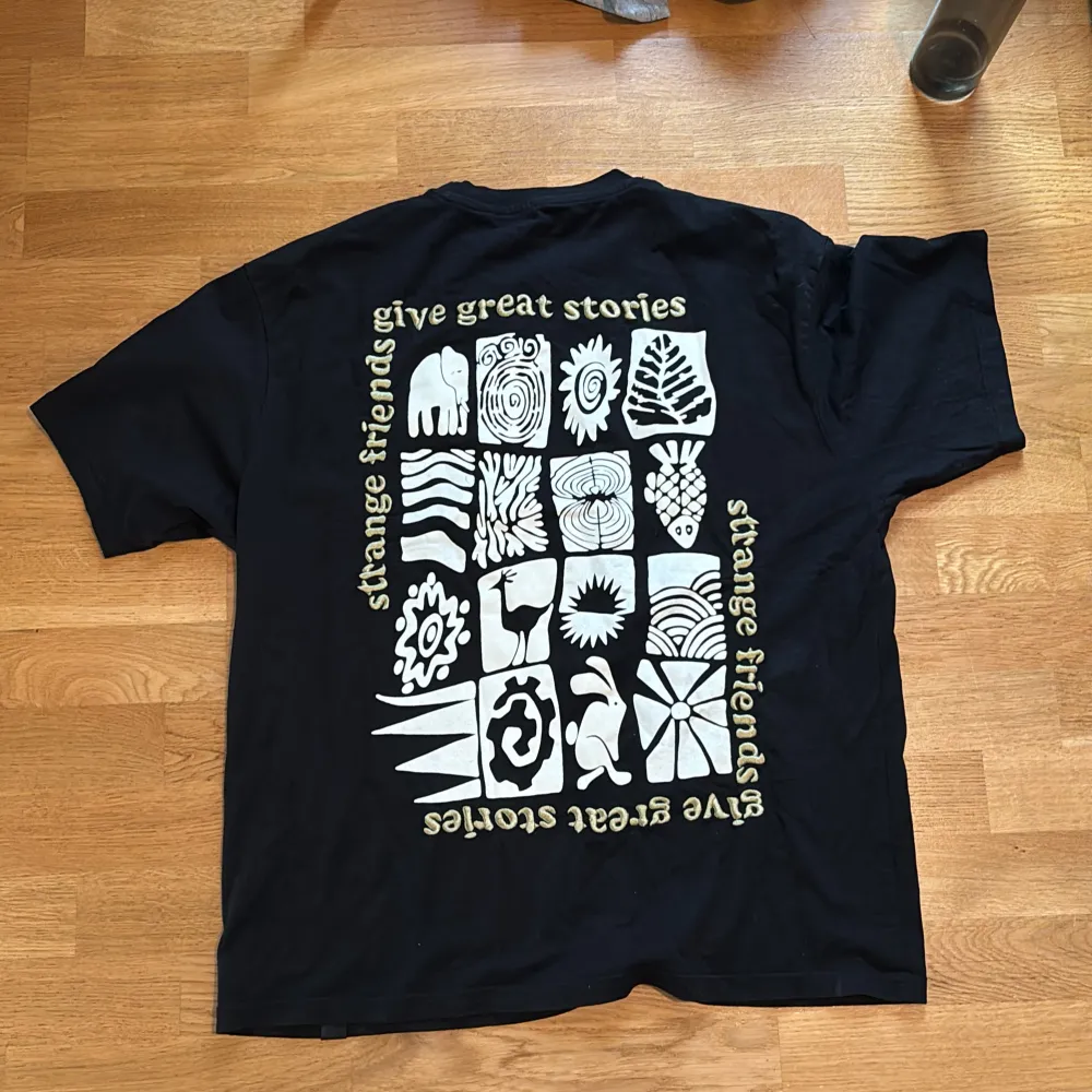 Säljer en svart t-shirt från Pull&Bear i storlek M. Den har en avslappnad passform och är gjord i mjuk bomull. På framsidan finns ett tryck med text och en grafisk design, och baksidan har ett större tryck med olika mönster och texten 'give great stories'. Perfekt för en casual look!. T-shirts.