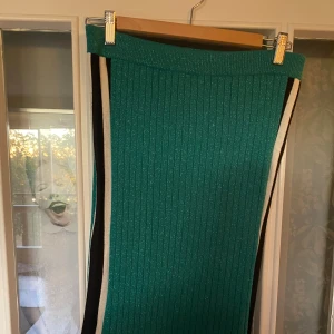 Grön ribbad kjol - Säljer en superfin grön ribbad kjol med svarta och vita ränder på sidorna. Kjolen har en tight passform och är perfekt för både vardag och fest. 