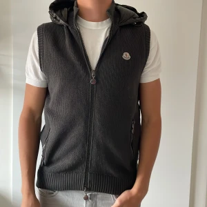 Grå stickad dunväst från Moncler - Säljer en snygg grå stickad dunväst från Moncler. Västen har en quiltad baksida och en praktisk huva. Äkthets bevis finns🤝Passar M. Skick 9/10. Pris: 3700kr🤝