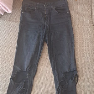 Svarta jeans med slitningar - Säljer ett par svarta jeans med coola slitningar på knäna. De har en tight passform och är perfekta för en avslappnad och trendig look. Jeansen har en klassisk femficksdesign och stängs med dragkedja och knapp. Perfekta för höst och vår!