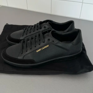 Svarta sneakers/skor från Saint Laurent - Säljer ett par stilrena svarta sneakers från Saint Laurent. De är i nyskick och tillverkade i Italien. Skorna har en klassisk design med snörning och är gjorda i skinn. Perfekta för både vardag och fest!  Köptes på farfetch för 6700 kr.