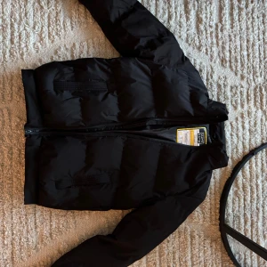 Svart pufferjacka från Superior - Säljer en svart pufferjacka från Superior. Den är perfekt för kalla dagar med sin vadderade design och dragkedja framtill. Aldrig använd