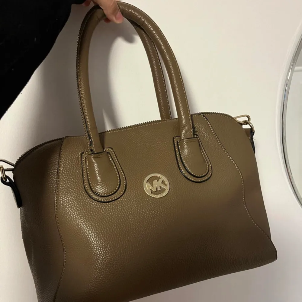 Säljer en snygg brun handväska från Michael Kors i skinn. Väskan har en stilren design med ett stort fack och dragkedja upptill. Perfekt för både vardag och fest! . Väskor.