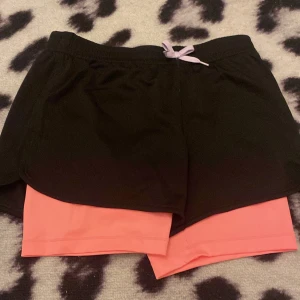 Rosa insydda shorts i svarta shorts  - Fina träning shorts, fint och rent skick, inte trasig, lila rosett, använd 2 gånger. Pris går att diskutera. 
