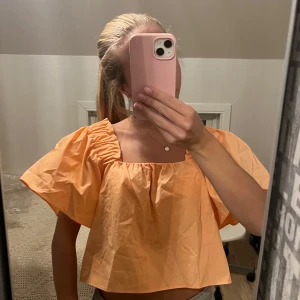 Orange croppad topp - Säljer en superfin orange croppad topp med puffiga kortärmar. Perfekt för sommardagar eller en festlig kväll. Toppen har en lös passform och är gjord i ett lätt material som känns skönt mot huden. Passar perfekt med ett par höga jeans eller en kjol. 🧡Den är tyvärr lite för stor för mig, men är i en otrolig färg!🥰