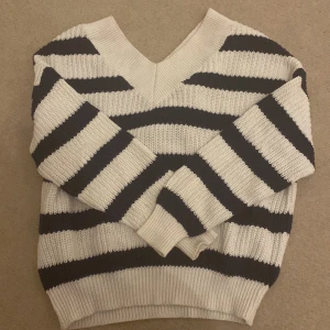 Randig stickad tröja - Säljer en supermysig stickad tröja med breda svarta och vita ränder. Den har en v-ringad hals och långa ärmar, perfekt för kyliga dagar. Tröjan är i bra skick och passar perfekt till både jeans och kjol. Perfekt för höst och vinter!