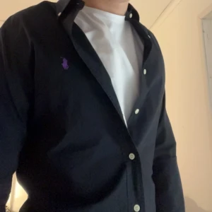 Svart skjorta från Ralph Lauren ( Storlek s )  - Säljer en svart skjorta från Ralph Lauren i storlek S och passar även så. Denna efterfrågade colorway är riktigt unik. Skjortan har en slim passform och har ett lila märke. Skick är 10/10, den är inprincip ny utan prislapp🙌🏼. Frakt på 1-2 dagar ✅📦!