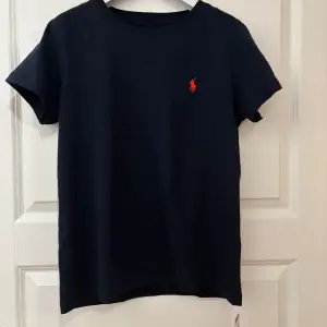 Hej 👋🏼 Säljer en snygg mörkblå t-shirt från Polo Ralph Lauren i storlek S. Den är ny och har kvar prislappen! Den har en klassisk design med det ikoniska röda logotypbroderiet på bröstet. Perfekt för en stilren och avslappnad look. Hör gärna av er om ni har några frågor😃