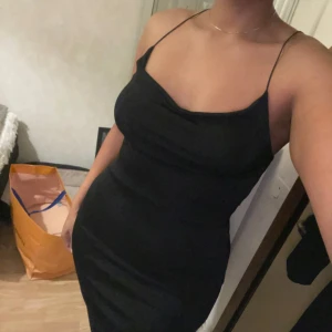 Svart klänning med tunna axelband - Snygg svart klänning med tunna axelband, perfekt för festliga tillfällen. Den har en tight passform som framhäver figuren och är tillverkad i ett mjukt och bekvämt material. Klänningen är ärmlös och har en stilren design som gör den lätt att matcha med olika accessoarer.