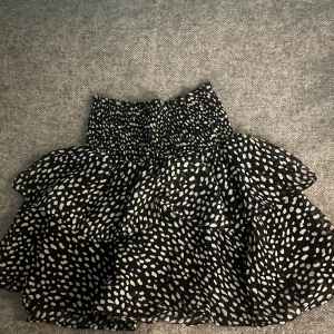 Svart och vit prickig kjol - Säljer en superfin svart och vit prickig kjol med volanger. Den har en elastisk midja som gör den bekväm och lätt att bära. Perfekt för både vardag och fest! 🖤🤍Ser kanske liten ut, men passar allt från XS-L eftersom att midjan är extremt elastisk.