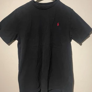 Svart t-shirt från Ralph Lauren - Säljer en klassisk svart t-shirt från Ralph Lauren i storlek S. Den har en liten röd broderad logga på bröstet. Perfekt för en stilren och avslappnad look. Pris 300kr